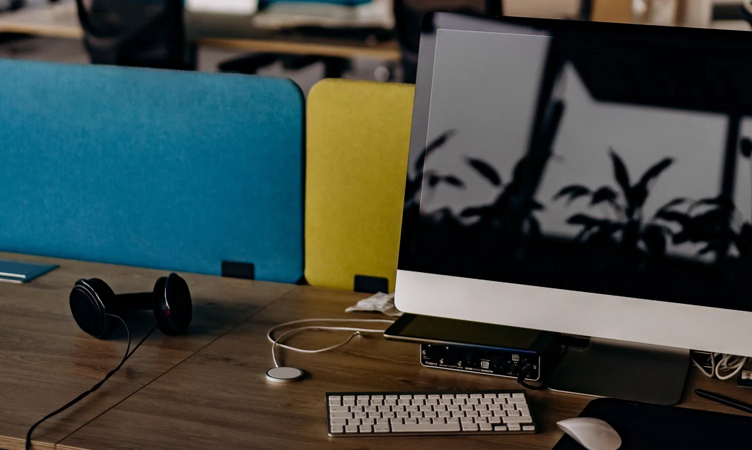 Estação de trabalho em escritório aberto, com monitor, teclado e fones sobre a mesa